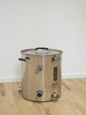 A stainless steel brewing kettle with custom gemstone fittings sits near a white wall in an art gallery.