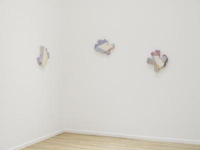 Three colourful ceramic forms hang on two perpendicular white walls.