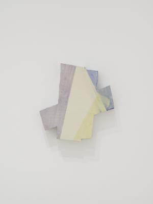 A ceramic form hangs on a white wall. Its shape resembles two intersecting rectangles. Areas are painted in overlapping purple, blue, and yellow glaze using a masking technique.