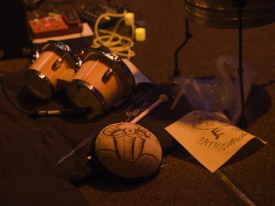 A set of bongos, a mallet and drumsticks, a sheet of bubble wrap, effects pedals, and two drawings are positioned on the floor of the Grand Luxe Hall.