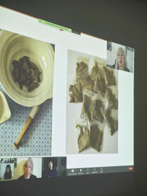 A Zoom meeting is projected on the wall. A photo of a mortar and pestle with clay inside are shown next to an image of baggies holding powdered clay.