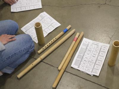 An aerial shot of instruments and sheets of paper on the ground. The paper reads Udlot-Udlot, followed by a musical score displaying all instrument parts at once.