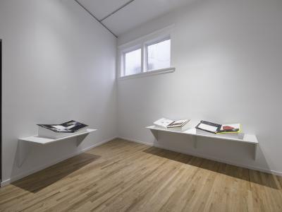 A white cube gallery with three mixed-media artist books lying open on plinths.