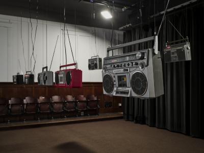  A row of five radios hang from the ceiling with their power chords climbing up to the ceiling. The closest radio reads TOSHIBA and just below, AUTO REVERSE.
