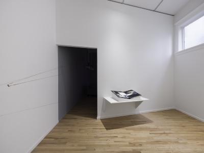 A white-cube gallery with a mixed-media artist book open on a plinth.