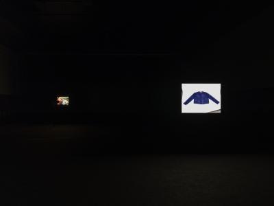 A portrait of the artist’s grandmother and a photograph of a blue jacket laid on a table are projected on screens in a darkened room. 