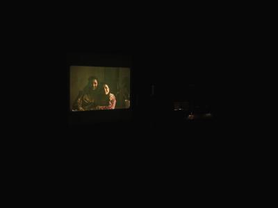 An analogue photograph of two women with their arms around each other is projected on a screen in a dark room.