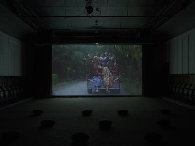 Ten people crowd the back of a pickup truck wearing traditional Filipino garments. Eight figures have their hands up in rejoice while Bhenji Ra rests her head on her grandmother's shoulder. This is the focal point of the image.