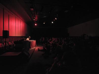 Phew is lit by a soft red light in the darkened Grand Luxe Hall. The light defines the edges of bodies occupying the front rows of the audience. Bent over the technology covered table in front of her, Phew’s short hair falls forward, obscuring her face.