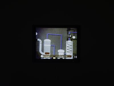 A projected still illuminated in a dark room, featuring an animation of old factory machinery with accompanying captions.