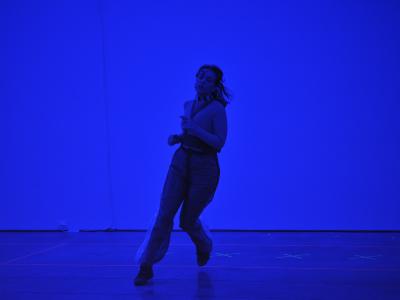 Nour Mobarak runs in a gallery flooded with blue light. Her left foot is barely tapping the floor while her right foot remains lifted in motion. 