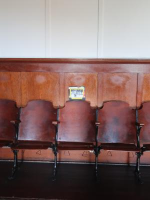 Five empty brown chairs line the walls of the Grand Luxe Hall. A small collage sits atop the chair in the middle.

