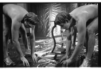 Brian Routh and Martin von Hasselberg stand facing each other while bending over to touch the floor of the Grand Luxe Hall, which is covered in a tarp-like material.