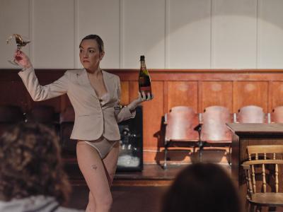 Marie Segolene Brault bites her lip while holding an open champagne bottle labeled PIPER HEIDSIECK in one hand and a martini glass spilling liquid in the other.