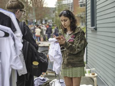 Katayoon Yousefbigloo processes a transaction using her phone. She wears a camouflage hoodie printed with the Liquidation World logo. In the background, a long line forms down the street. 