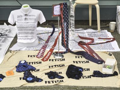 A display of screenprinted socks, ties, and tee shirts arranged on beige and white blankets on the sidewalk. A freestanding metal sign reads Everything Must Go. 
