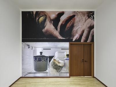 A wallpaper with a diptych image spans from floor to ceiling and wraps around a set of wood double doors. The top image shows a glamorous Chinese grandmother with gold eyeshadow and a shiny red lip. Below is a photo of leftovers sitting in a refrigerator. 