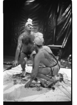 Martin von Hasselberg and Brian Routh crouch on a white tarp in the Grand Luxe Hall. They wear swim caps, goggles, and jockstraps, and are streaked in various liquids. They each have a squirt of shaving cream on their heads.