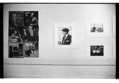 Nine photos of jazz musicians are nailed directly to the gallery wall. Six of the images are album covers arranged in a tight grid. The remaining three are portraits printed with thick white boards. 