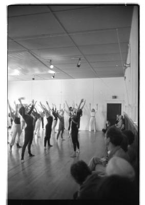 A group of dancers stand in rows with their arms energetically extended upwards. 