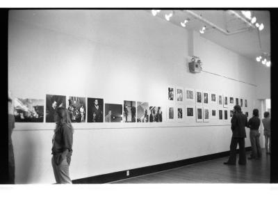 Photographic prints of jazz musicians are hung in rows on the gallery walls. Several visitors contemplate the prints.