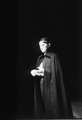 Jeanette Reinhardt wears a black head covering and a black cape. She pulls on the fingers of her white gloves to remove them.