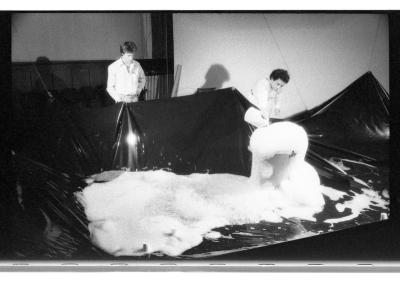 Hank Bull stands next to Alzek Misheff as he pours more bubble solution onto an already overflowing bin of bubbles. A plastic tarp catches the fill.