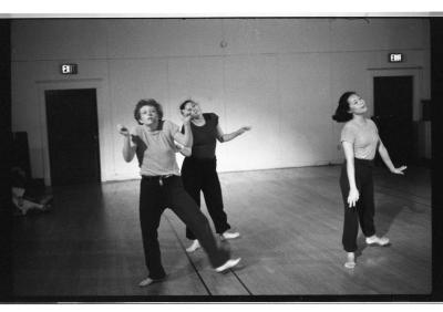 A black-and-white photo showing Susan McKenzie, Paula Ravitz, and Denise Fujiwara dancing. They look like they’re shrugging. They’re all barefoot and wear t-shirts and sweatpants.