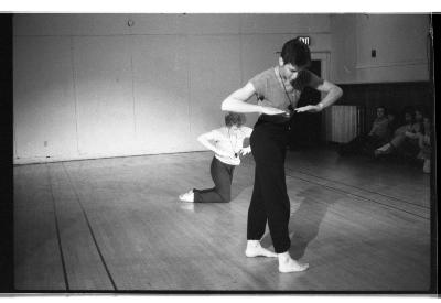 A black-and-white photo showing Seth Levinson 
standing with his elbows bent and palms facing the floor. Behind him, Susan McKenzie mirrors this posture while kneeling.