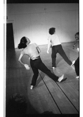 A black-and-white photo showing Denise Fujiwara and Susan McKenzie dancing in sync with their backs to the camera. Their weight is on their left leg, while their right foot is flexed upwards.