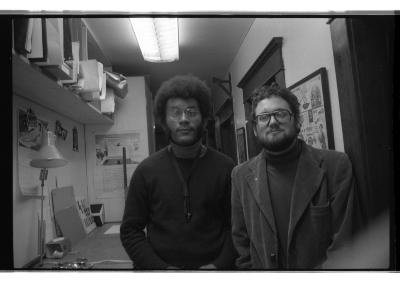Anthony Braxton and Eugene Chadbourne stand next to each other in what is now Western Front’s media hall. Braxton’s saxophone is seen placed on the countertop along the hallway. They both gaze directly into the camera.