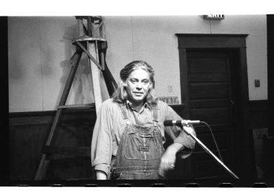  Standing with one hand on a podium and the other in motion, the author gestures down.