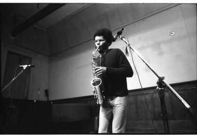 Staring ahead at the audience, the musician presses down on the saxophone’s buttons.