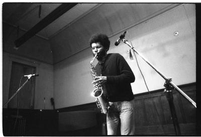 The saxophone reflects the stage lights as the musician strategically blocks one hole close to the top of the instrument. 