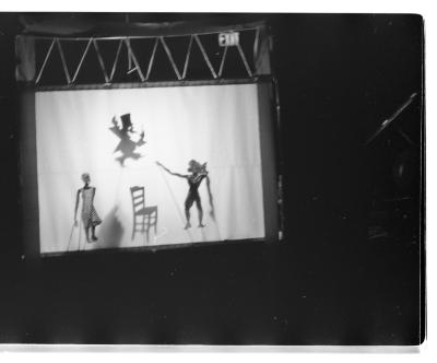 A portable shadow theatre depicts three shadow puppet figures and a shadow puppet chair.