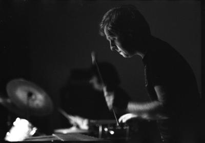 Paul Plimley plays the xylophone with vigour. His lips are pursed and he holds a mallet in each hand, while looking concentrated at the instrument. 