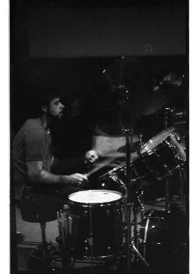 Seen in profile, Paul Grant plays a drum kit. His movements create a slight motion blur around his hands. The image is in black and white.