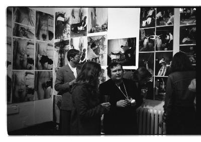 Vincent Trasov, Cornelia Wyngaarden, and Herman Nitsch stand in front of a photographic installation in the gallery. 