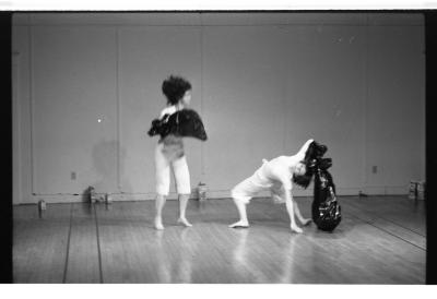 A black-and-white photo of Jane Ellison and Lin Bennett dancing with garbage bags in the EDAM Studio. Jane is captured as a blur in mid motion, while Lin is seen in a backbend.